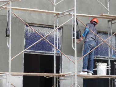 Kuala Lumpur, Malezya-23 Ağustos 2018: çimento alçı kullanarak inşaat işçileri tarafından sıvalı tuğla duvar. İskele geçici evreleme olarak yükseklikte çalışırdım. Kötü olmasını önlemek için uygun güvenlik dişli giyiyor.  
