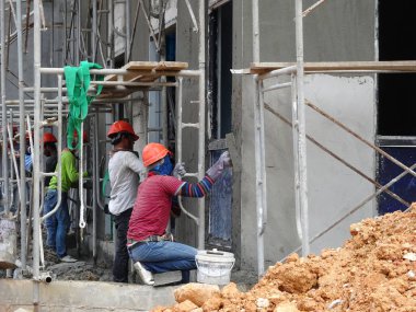 Kuala Lumpur, Malezya-23 Ağustos 2018: çimento alçı kullanarak inşaat işçileri tarafından sıvalı tuğla duvar. İskele geçici evreleme olarak yükseklikte çalışırdım. Kötü olmasını önlemek için uygun güvenlik dişli giyiyor.  