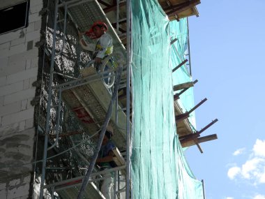 Kuala Lumpur, Malezya-23 Ağustos 2018: çimento alçı kullanarak inşaat işçileri tarafından sıvalı tuğla duvar. İskele geçici evreleme olarak yükseklikte çalışırdım. Kötü olmasını önlemek için uygun güvenlik dişli giyiyor.  