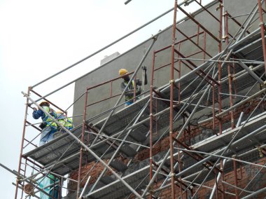 Kuala Lumpur, Malezya-23 Ağustos 2018: çimento alçı kullanarak inşaat işçileri tarafından sıvalı tuğla duvar. İskele geçici evreleme olarak yükseklikte çalışırdım. Kötü olmasını önlemek için uygun güvenlik dişli giyiyor.  