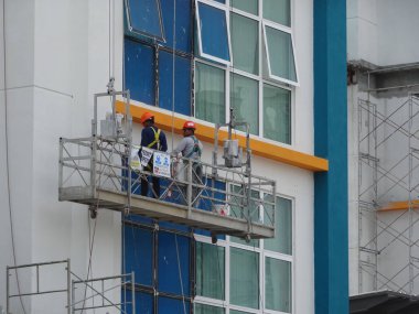 KUALA LUMPUR, MALAYSIA - 16 Mart 2017: İşçiler bir servis gondolu kullanarak binanın içini temizleme ve bakım sürecindeler. Güvenlik önlemi olarak emniyet kemeri takıyorlar..