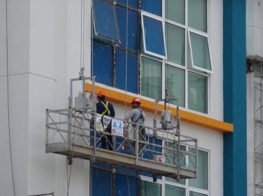 KUALA LUMPUR, MALAYSIA - 16 Mart 2017: İşçiler bir servis gondolu kullanarak binanın içini temizleme ve bakım sürecindeler. Güvenlik önlemi olarak emniyet kemeri takıyorlar..