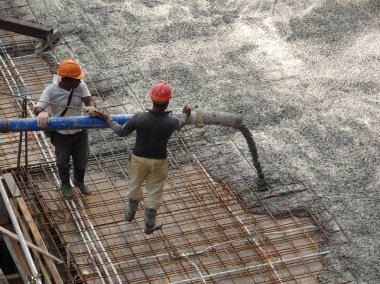 KUALA LUMPUR, MALAYSIA -JANUARY 16, 2018: Construction workers pouring wet concrete using concrete spider hose into floor slab form work at the construction site.  clipart