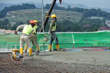 MALACCA, MALAYSIA -17 Haziran 2016: İnşaat işçileri inşaat alanında yere dökülen ıslak betonu yerle bir ediyorlar.