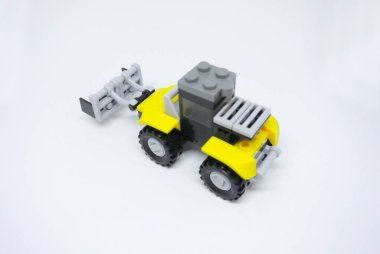 Sarı ve siyah plastik tuğlalardan yapılmış oyuncak buldozer ve beyaz arka planda izole edilmiş tekerlekler..