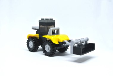 Sarı ve siyah plastik tuğlalardan yapılmış oyuncak buldozer ve beyaz arka planda izole edilmiş tekerlekler..