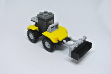 Sarı ve siyah plastik tuğlalardan yapılmış oyuncak buldozer ve beyaz arka planda izole edilmiş tekerlekler..
