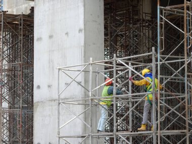 KUALA LUMPUR, MALAYSIA - MAYIS 05, 2016: İskeleye tırmanırken emniyet kemeri ve yeterli güvenlik teçhizatı takan inşaat işçileri. Bu, yüksek seviyede çalışırken güvenliklerini sağlamak için.. 