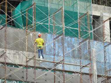 KUALA LUMPUR, MALAYSIA - MAYIS 05, 2016: İskeleye tırmanırken emniyet kemeri ve yeterli güvenlik teçhizatı takan inşaat işçileri. Bu, yüksek seviyede çalışırken güvenliklerini sağlamak için.. 