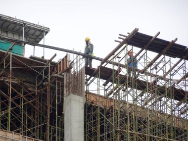 KUALA LUMPUR, MALAYSIA - MAYIS 05, 2016: İskeleye tırmanırken emniyet kemeri ve yeterli güvenlik teçhizatı takan inşaat işçileri. Bu, yüksek seviyede çalışırken güvenliklerini sağlamak için.. 