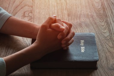 İncil 'de dua eden bir kadın, elleri ahşap masada İncil' ine kenetlenmiş..