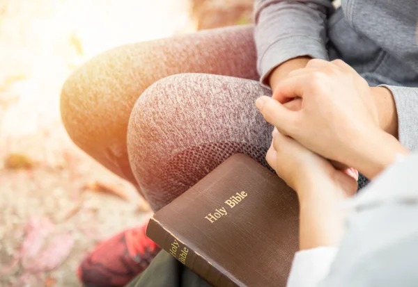 Two women hold hands and pray as they study the bible. Christian concept.