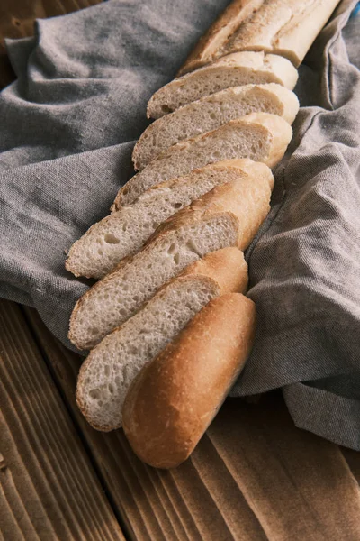 Close up fresco baguete francês fatiado em um pano de linho em uma mesa de madeira — Fotografia de Stock