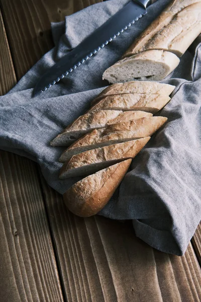 Close up fresco baguete francês fatiado em um pano de linho com faca em uma mesa de madeira — Fotografia de Stock