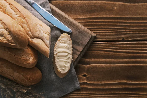 Vista superior fresco baguete francês fatiado com manteiga em um pano de linho com faca em uma mesa de madeira — Fotografia de Stock