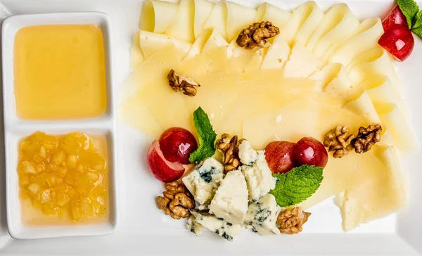 Variedad de quesos en un plato cuadrado de cerámica con limón y nueces de miel — Foto de Stock