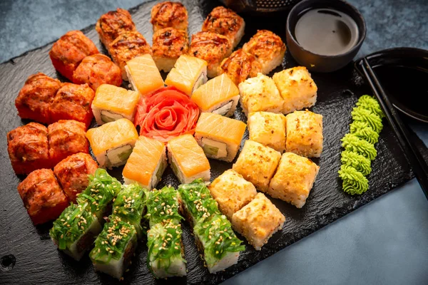 Set de rollos de sushi servidos sobre pizarra de piedra negra sobre fondo oscuro. Menú japonés. Vista superior horizontal desde arriba — Foto de Stock