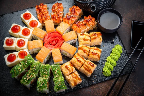Set de rollos de sushi servidos sobre pizarra de piedra negra sobre fondo oscuro. Menú japonés. Vista superior horizontal desde arriba — Foto de Stock