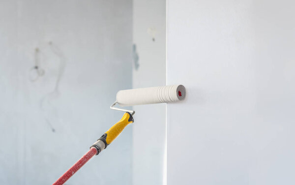 Paint roller applying paint on white wall, home improvements.
