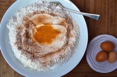 Baharatlı bir tabak un ve ahşap bir masada üç yumurta daha.