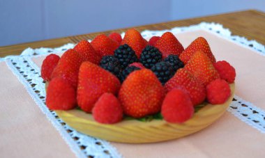 Ahşap masadaki somon masa örtüsünün üzerinde böğürtlen ve böğürtlen tabağı