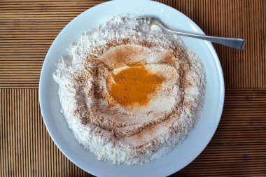 Tahta çizgili bir masanın kenarına bir kaşık dolusu un, zerdeçal, kırmızı biber, tarçın gibi baharatlar.