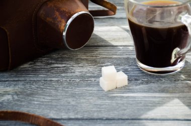 Ahşap arka planda bir fincan kahve ve kruvasanla sakin bir hayat. Eski kamera ve kartpostal bardağın yanında..