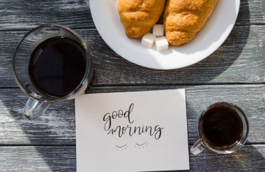 Ahşap arka planda bir fincan kahve ve kruvasanla sakin bir hayat. Eski kamera ve kartpostal bardağın yanında..