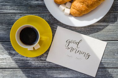 Ahşap arka planda bir fincan kahve ve kruvasanla sakin bir hayat. Eski kamera ve kartpostal bardağın yanında..