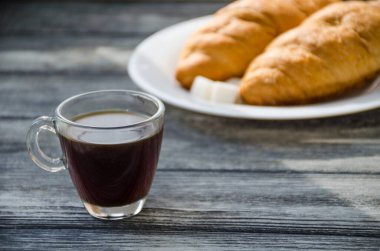 Ahşap arka planda bir fincan kahve ve kruvasanla sakin bir hayat. Eski kamera ve kartpostal bardağın yanında..