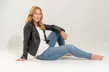 Kot pantolon ve fermuarlı deri ceket giymiş sarışın genç bir kadın.