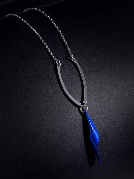 Siyah zemin üzerinde mavi mücevher ve kağıt desenli kolye.