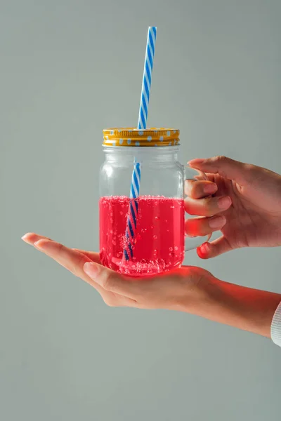 Kadının elleri mavi pipetli cam tutuyordu. Gri arka planda pembe sıvı vardı.