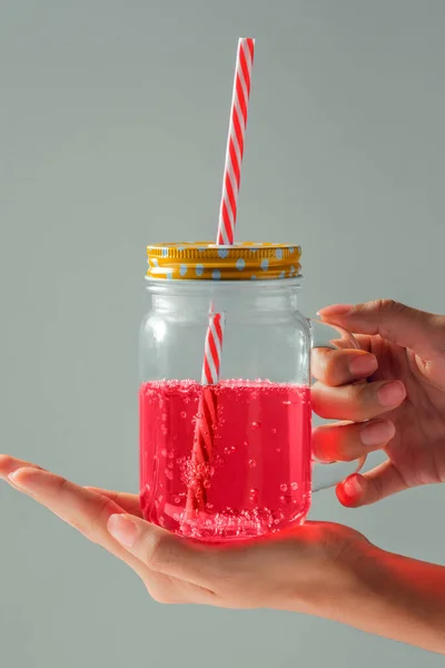 Kadının elleri mavi pipetli cam tutuyordu. Gri arka planda pembe sıvı vardı.