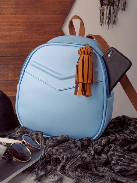 Üzerinde siyah cep telefonu olan gri eşarplı mavi deri bir sırt çantası ve ahşap kaplama ve beyaz duvarlı dergiler.