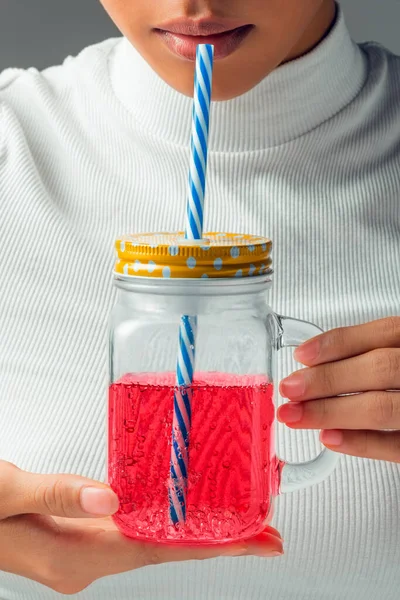 Beyaz bluzlu kadın elinde bardakla pipetten içiyor gri arka planda pembe bir sıvı.