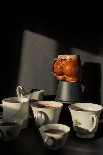 Günbatımı penceresinde siyah bir arka planı olan kışkırtıcı kadın şeklindeki bir fincanın etrafında klasik çay fincanları.
