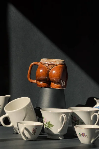 Günbatımı penceresinde siyah bir arka planı olan kışkırtıcı kadın şeklindeki bir fincanın etrafında klasik çay fincanları.