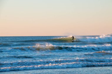 Güneşli bir sörfçünün tadını çıkaran sörfçü, San Francisco yakınlarında günbatımında sörf yapıyor.