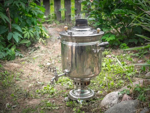 Smoking russian samovar standing on the ground in sunny summer garden