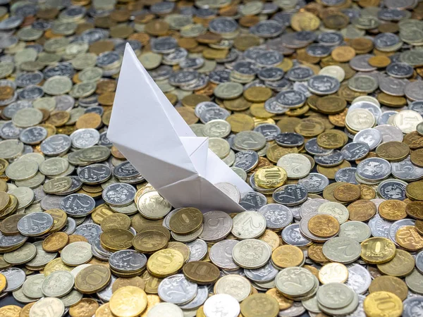 White paper boat sinking in sea made from coins. Origami ship shipwrecked in russian coins of various denominations: rubles and kopecks. Selected focus.