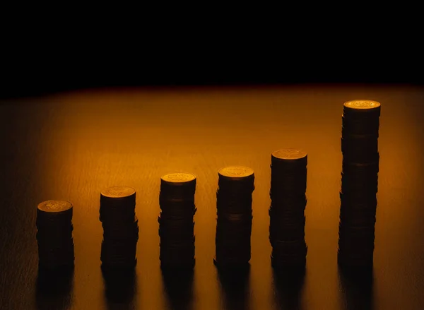 Silhouettes of coin stack isolated on dark background. Stacks of coins of various heights. Vertical bar chart.