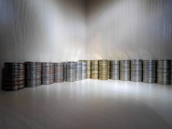 Stacks of coins in corner of the wooden box. Coin stacks of different high on dark wooden background.