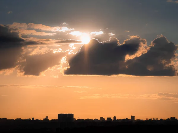 Buildings silhouettes over forest on sunset twilight and orange tone sky with long clouds as background in evening haze with rays from sun behind clouds. Sunny weather (Moscow city, Russia)