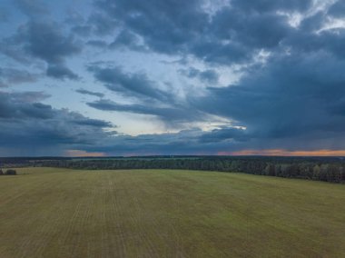Ufukta alan ve çok karanlık orman ile kırsal üzerinde destansı bulutlar ile dramatik gökyüzü. Gün batımında bulutlu gökyüzü altında tipik kırsal manzara havadan görünümü. Moskova bölgesi, Rusya Federasyonu.