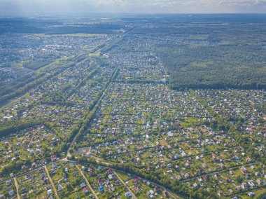 Yaz mevsiminde köyün insansız hava aracı manzarası. Evlerin çatıları, yeşil çimenleri ve ağaçlarla çevrili çiftlikler. Yolların ve göletin kuş bakışı manzarası. Moskova bölgesi, Rusya.