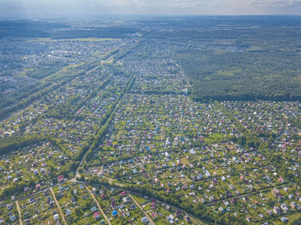Yaz mevsiminde köyün insansız hava aracı manzarası. Evlerin çatıları, yeşil çimenleri ve ağaçlarla çevrili çiftlikler. Yolların ve göletin kuş bakışı manzarası. Moskova bölgesi, Rusya.