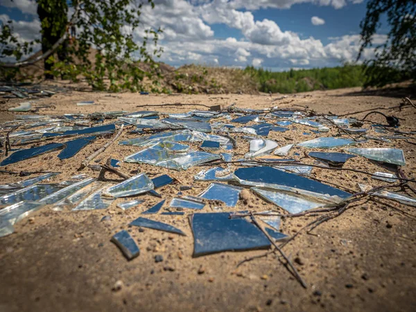 Fragments of a broken mirror on the ground with reflection of blue sky. Mirror shards on a dry soil. Perspective view, selected soft focus. Summer sunny day.