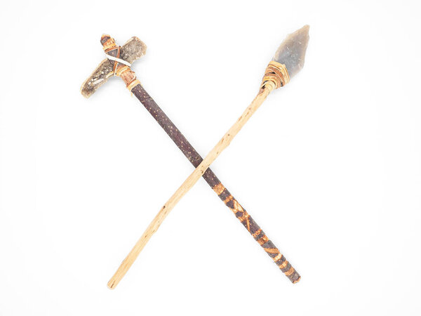 Replicas of the primal stone tools with wooden handles and leather strapping isolated on white background. Crossed primitive stone axe and dagger or spear: weapons of the prehistoric peoples.