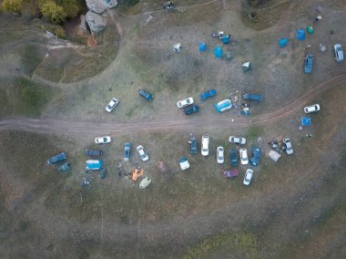 Çim tarlasında turist kampı. Kamp alanının havadan aşağı görüntüsü. Yol kenarında çadır ve araçlar var. Çok renkli turistik evler ve arabalar. Yaz mevsiminde otokopi kavramı.